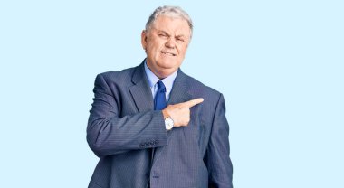 İş ceketi giyen yaşlı, gri saçlı bir adam endişeli ve endişeli bir ifade takınıyor. 