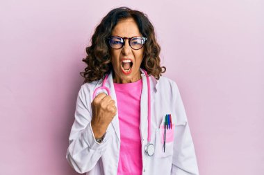 Orta yaşlı İspanyol kadın doktor üniforması giyiyor ve gözlük takıyor kızgın ve kızgın yumruğunu kaldırıyor ve öfkeyle bağırıyor. öfke ve agresif konsept. 