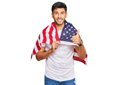 Young handsome man holding united states flag smiling happy and positive, thumb up doing excellent and approval sign 