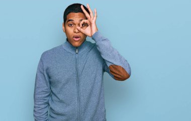 Genç, yakışıklı, sıradan bir tişört giyen, şaşırmış yüzüyle şaşırmış, parmaklarının arasından bakan Latin asıllı bir adam. İnançsız ifade. 