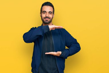 Latin asıllı genç adam, sıradan kıyafetler giyiyor. Elleriyle işaret ediyor. Ölçü sembolü, büyük boy işareti. Kameraya bakıp gülümsüyor. ölçüm kavramı. 