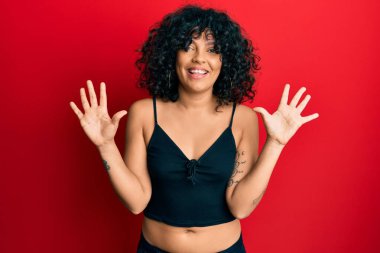 Kolsuz tişörtlü, gündelik giyinen genç İspanyol kadın on numaralı parmaklarıyla kendini beğenmiş ve mutlu gülümserken onu işaret ediyor.. 