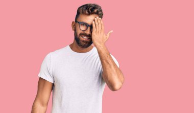 Gündelik kıyafetler ve gözlük takan genç İspanyol bir adam bir gözünü eliyle kapatıyor, yüzünde kendine güvenen bir gülümseme ve sürpriz bir duygu var.. 