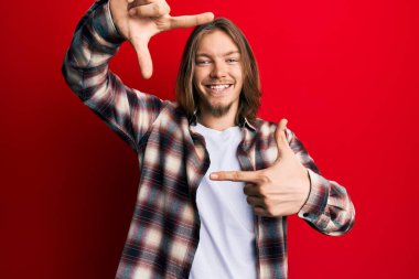 Yakışıklı, beyaz, uzun saçlı, günlük kıyafetler giyen, gülümseyen, elleri ve parmakları gülen yüzlü bir adam. yaratıcılık ve fotoğrafçılık kavramı. 