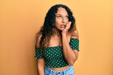 Günlük kıyafetler giyen genç Latin kadın gergin ve gergin görünüyor. Ağzı tırnak yiyen ellerle. anksiyete. 