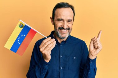 Orta yaşlı İspanyol adam Venezuela bayrağını tutuyor. Gülümsüyor, mutlu bir şekilde işaret ediyor. 
