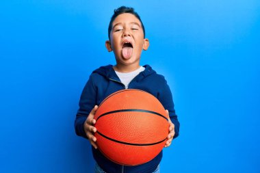 Küçük İspanyol çocuk basketbol topu tutuyor. Dilini komik bir ifadeyle dışarı çıkarıyor.. 