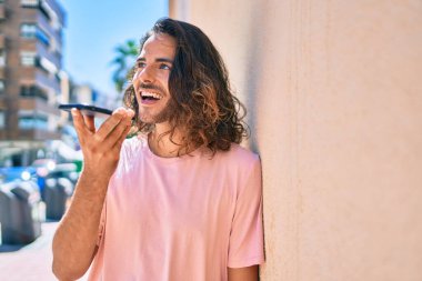 Genç İspanyol adam gülümsüyor. Akıllı telefonda konuşuyor. Duvara yaslanıyor.