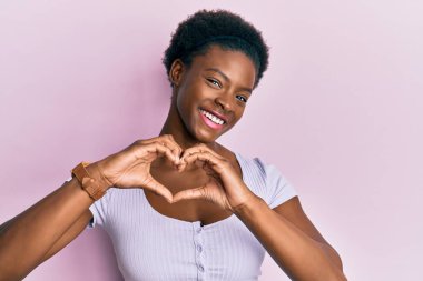 Genç Afro-Amerikan kızı, gündelik giysiler giyip aşıkken gülümsüyor. Elleriyle kalp sembolü yapıyor. romantik kavram. 