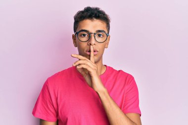 Pembe arka planda gözlüklü Afro-Amerikan genç adam sessiz olup dudaklarını öpmek istiyor. sessizlik ve gizli konsept. 