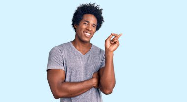 Yakışıklı Afro saçlı, sıradan kıyafetler giyen, yüzünde kocaman bir gülümseme olan eli ve parmağı kameraya bakan Afro-Amerikan bir adam.. 