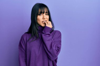 Kâküllü, balıkçı yaka kazak giyen genç esmer kadın gergin ve elleri ağızda tırnak yerken gergin görünüyor. anksiyete. 