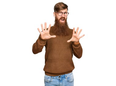 Young irish redhead man wearing casual clothes and glasses afraid and terrified with fear expression stop gesture with hands, shouting in shock. panic concept. 