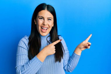 Güzel esmer kadın, günlük kıyafetler giyiyor gülümsüyor ve kameraya bakıyor. İki eliyle ve parmaklarıyla kenarı işaret ediyor.. 