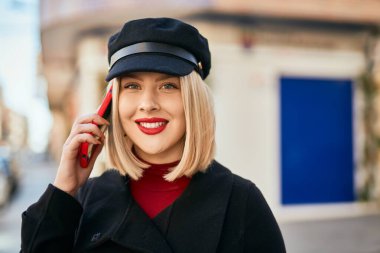 Genç sarışın kadın gülümsüyor. Şehirdeki akıllı telefondan konuşuyor..