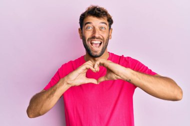 Sakallı yakışıklı adam elleri şekilli kalp sembolü yapıyor. Çılgınca kutlama yapıyor ve başarı için hayrete düşüyor. Gözleri açık, heyecanlı çığlıklar atıyor.. 