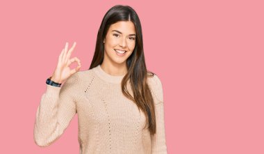 Kışlık süveter giyen genç esmer kadın gülümsüyor ve el ve parmaklarıyla 