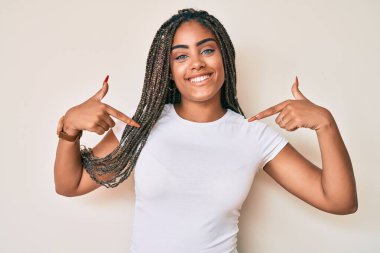 Örgülü beyaz tişörtlü, kendine güvenen, gülümseyen, kendini gururlu ve mutlu gösteren genç Afro-Amerikan kadını.. 
