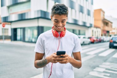 Genç Latin adam şehirde akıllı telefon ve kulaklık kullanarak mutlu bir şekilde gülümsüyor..