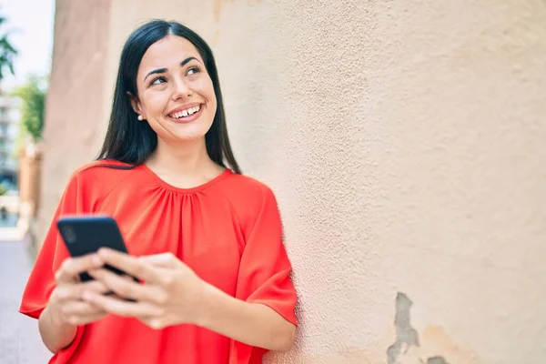 若いですラテン語の女の子笑顔幸せな使用してスマートフォンで市 — ストック写真