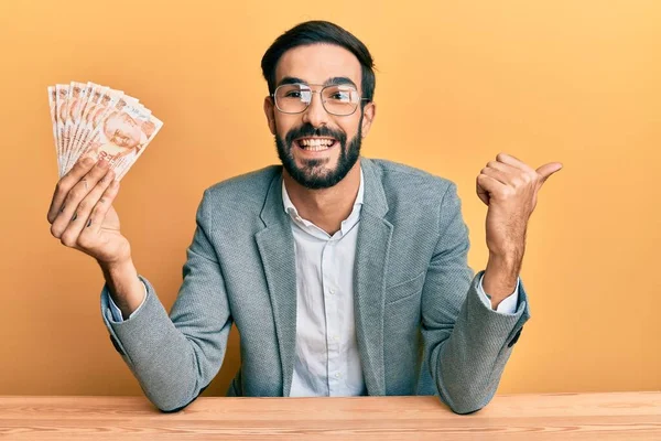 若いヒスパニック系の男を保持トルコのリラ紙幣テーブルの上に座って親指を指す側に幸せな笑みを浮かべて口を開けて — ストック写真