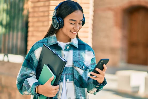 若いラテン語の学生の女の子笑顔幸せな使用してスマートフォンやヘッドフォンで街 — ストック写真