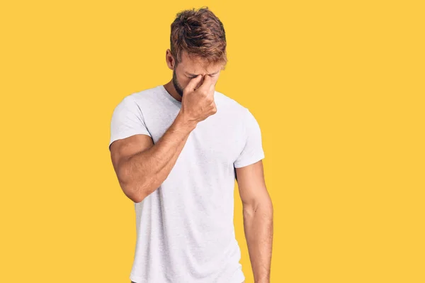 カジュアルな白いTシャツを着た若い白人男性が鼻をこすり 目は疲労と頭痛を感じます ストレスとフラストレーションの概念 — ストック写真