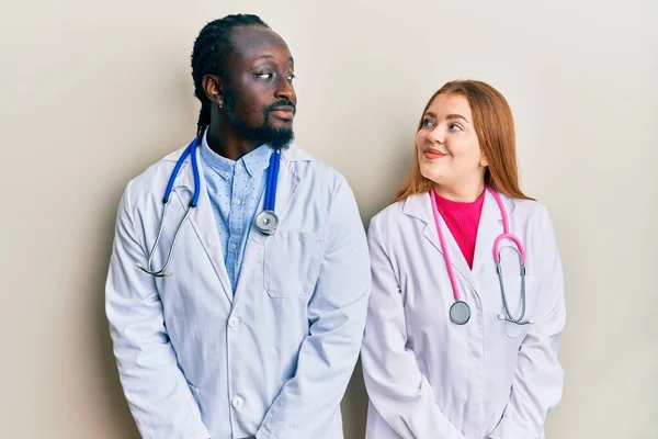 Joven Interracial Pareja Vistiendo Doctor Uniforme Estetoscopio Sonriendo Mirando Lado —  Fotos de Stock