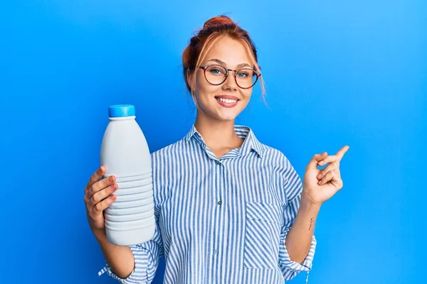 Молода Руда Жінка Тримає Літрову Пляшку Молока Посміхаючись Щасливо Вказуючи — стокове фото