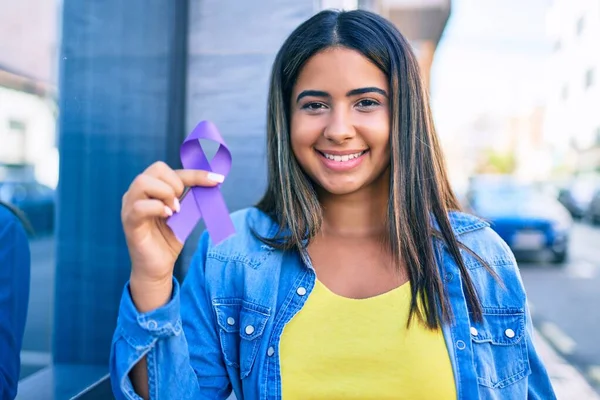 Young latin woman smiling happy holding purple ribbon at city.