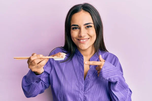 Joven Morena Comiendo Sushi Nigiri Usando Palillos Sonriendo Feliz Señalando —  Fotos de Stock