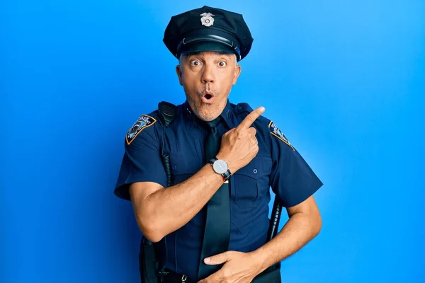 Handsome middle age mature man wearing police uniform surprised pointing with finger to the side, open mouth amazed expression.