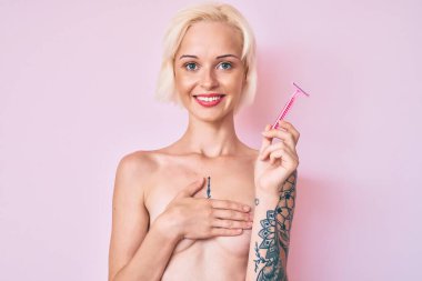 Dövmesi olmayan, yüzünde mutlu ve havalı bir gülümsemeyle jilet tutan genç sarışın kadın. diş gösterme. 