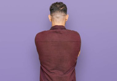 Gündelik kıyafetler giyen genç İspanyol adam arkasını dönüp kollarını kavuşturarak başka tarafa bakıyor. 