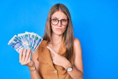 Güney Afrikalı Rand 'i elinde tutan genç sarışın kız şüpheci ve gergin, sorun yüzünden üzgün. negatif kişi. 