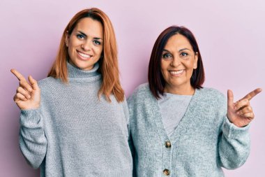 Latin anne ve kız günlük giysiler giyip neşeli bir gülümseme ile elleri ve parmaklarıyla mutlu ve doğal bir ifadeyle kenarı işaret ediyorlar. 