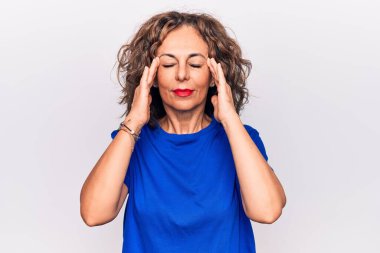 Orta yaşlı, güzel, esmer, mavi tişörtlü bir kadın. Beyaz arka plan üzerinde duruyor. Başı ağrıyor, çünkü stres var. Migren ağrısı..