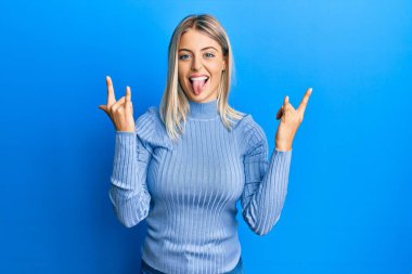 Güzel sarışın kadın gündelik kıyafetler giyip çılgın bir ifadeyle bağırıyor ve elleri havada rock sembolü yapıyor. Müzik yıldızı. ağır kavram. 