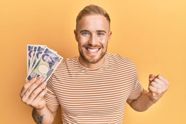Elinde Japon yen banknotları tutan genç beyaz adam gururla bağırıyor, zaferi ve başarıyı kutluyor. 