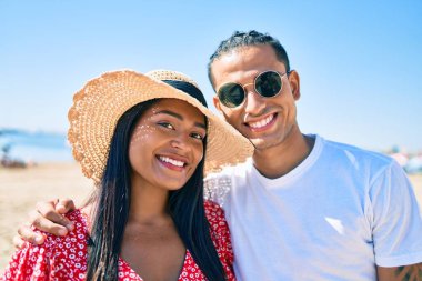 Genç Latin çift, mutlu bir şekilde gülümsüyor ve sahilde sarılıyorlar..