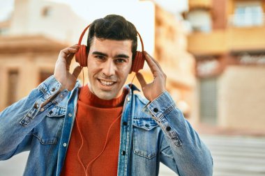 Şehirde kulaklık takarak mutlu gülümseyen genç İspanyol adam..