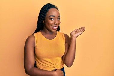 Genç Afro-Amerikan kadın, günlük giysiler giyip neşeli bir şekilde gülümseyerek el ele tutuşup kameraya bakıyor.. 