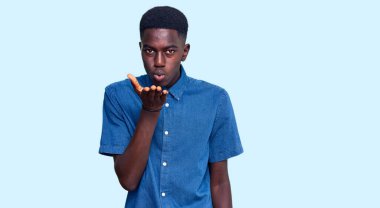 Gündelik giysiler giymiş genç Afro-Amerikan bir adam kameraya bakıp havada el ele öpüşerek sevimli ve seksi oluyor. aşk ifadesi. 