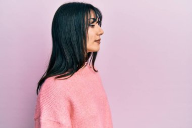 Kâküllü, kışlık süveter giyen genç esmer kadın yan yan yan bakıyor, rahat poz veriyor, kendine güvenen bir gülümsemesi var.. 