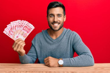 Yakışıklı İspanyol adam Yuan Çin banknotlarını tutuyor. Pozitif ve mutlu görünüyor. Kendine güvenen bir gülümsemeyle dişlerini gösteriyor. 
