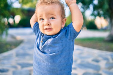 Sevimli ve mutlu küçük çocuk güneşli bir günde parkta eğleniyor. Güzel sarı saçlı erkek çocuk dışarıda oynuyor.