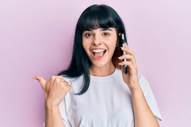 Genç İspanyol kız akıllı telefondan konuşuyor başparmağını kaldırıyor ve ağzı açık gülümsüyor. 