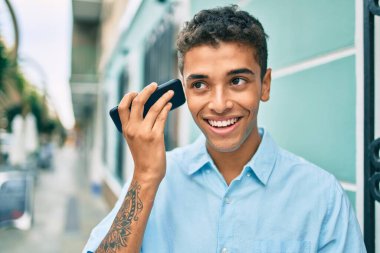 Genç Latin adam gülümsüyor. Şehirde akıllı telefon kullanarak mutlu bir sesli mesaj dinliyor..