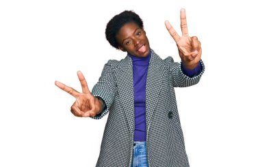 Gündelik giysiler giymiş, dili açık gülümseyen, zafer işareti yapan Afro-Amerikalı genç bir kız. İki numara.. 