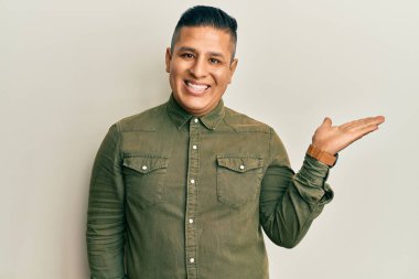 Gündelik kıyafetler giyen genç Latin adam neşeli bir şekilde gülümsüyor ve avuç içi kameraya bakıyor.. 